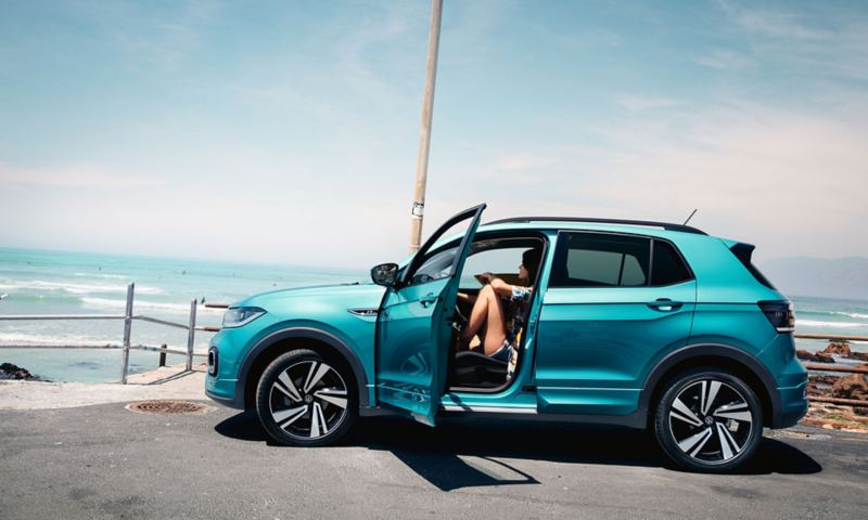 VW T-Cross bleu turquoise stationné devant la place avec la porte conducteur ouverte et une femme assise à cette place