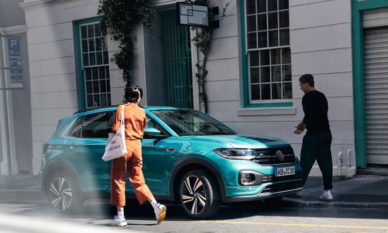 T-Cross Volkswagen parcheggiata in strada con uomo e donna che camminano per salire a bordo