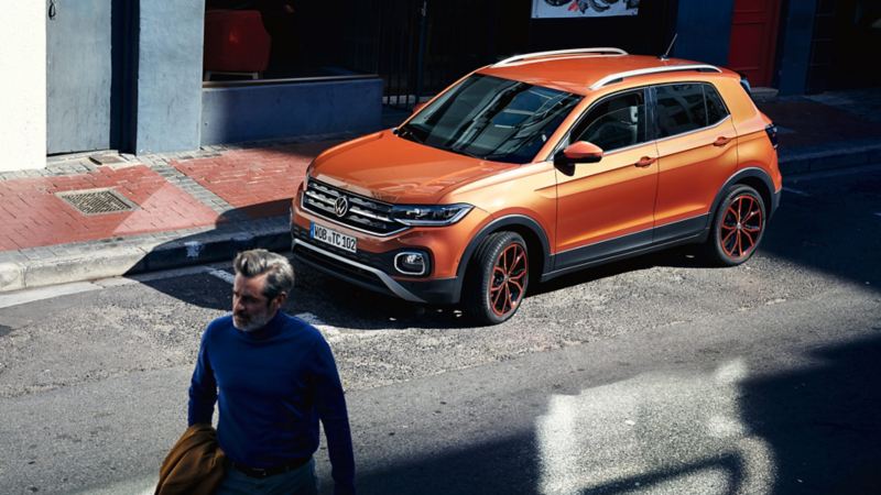 Une VW T-Cross dans une rue en ville en partie ombragée. Un homme se promène en avant-plan.