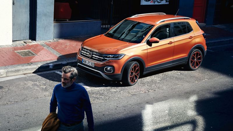 VW T-Cross holder delvist i skygge på vejen i en by, mens en mand går i forgrunden