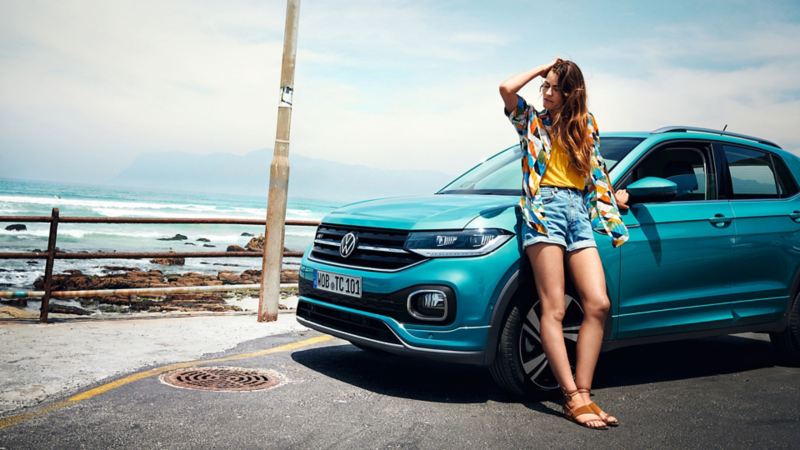Woman leaning against a VW T-Cross at a beach