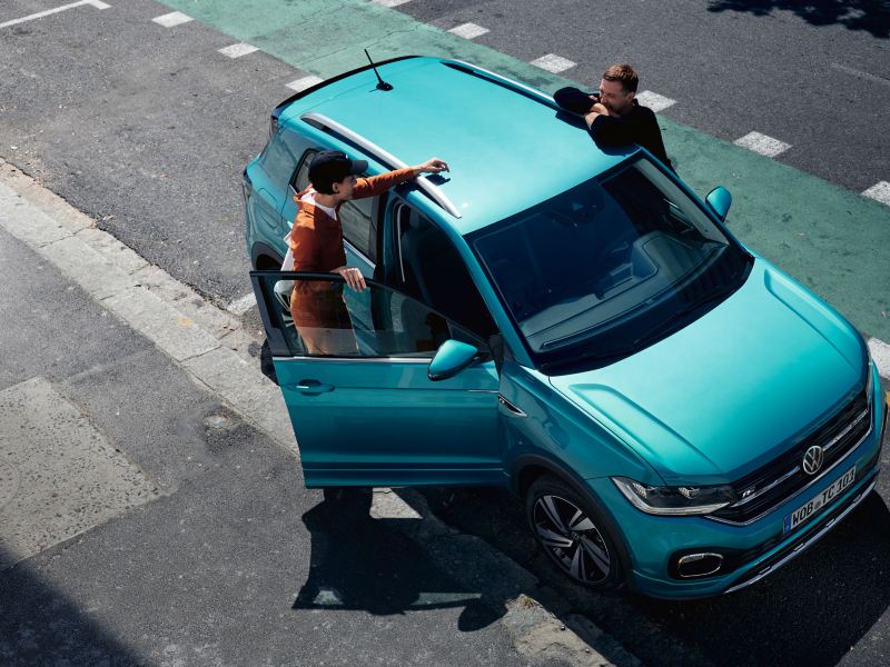 VW T-Cross turquoise vu d'en haut avec un couple qui discute entre les deux portières avant.