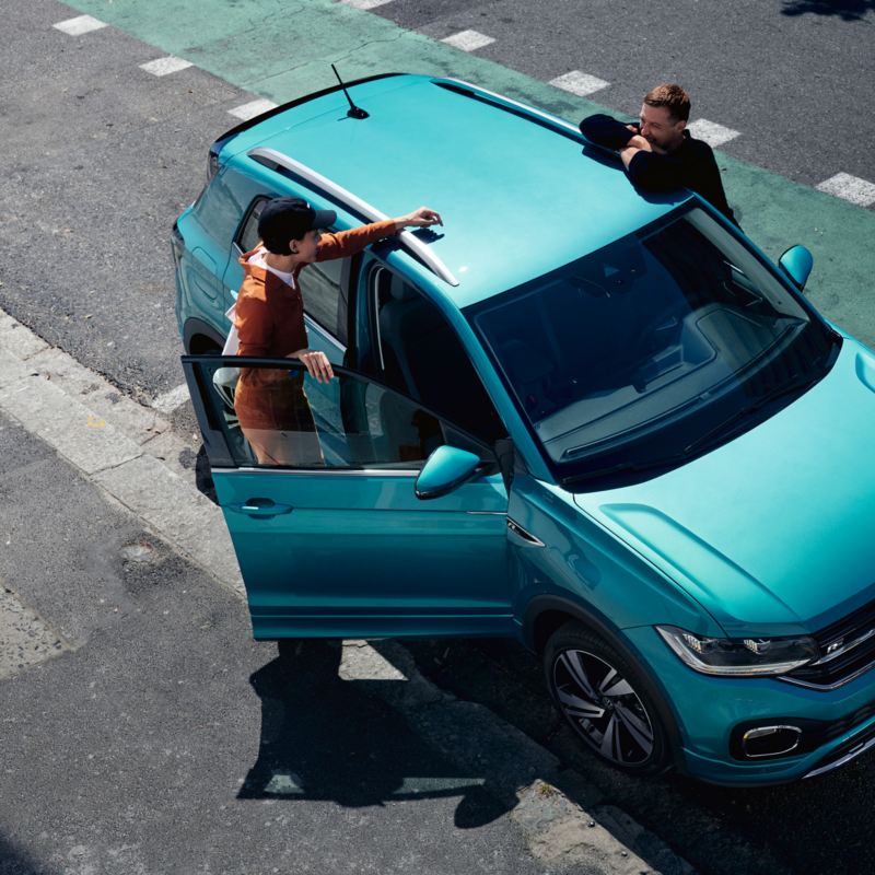 VW T-Cross turquoise vu d'en haut avec un couple qui discute entre les deux portières avant.