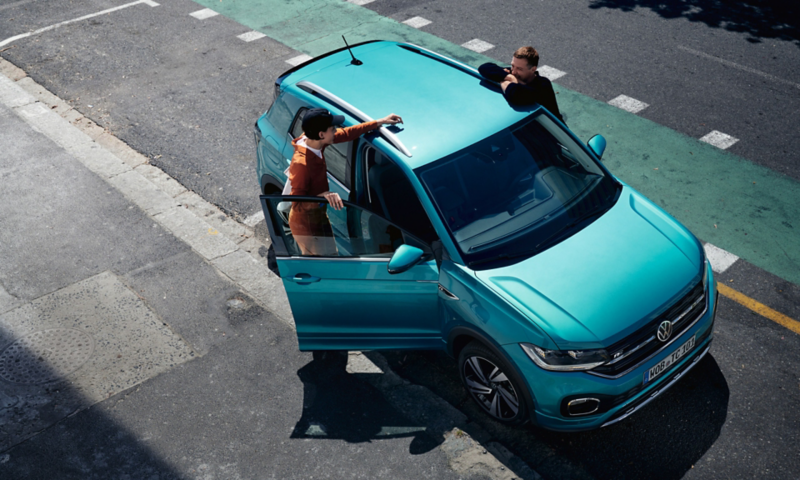 VW T-Cross turquoise vu d'en haut avec un couple qui discute entre les deux portières avant.