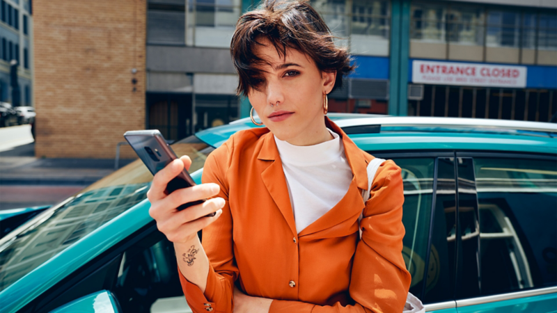 Woman holding a mobile phone standing in front of a T-Cross