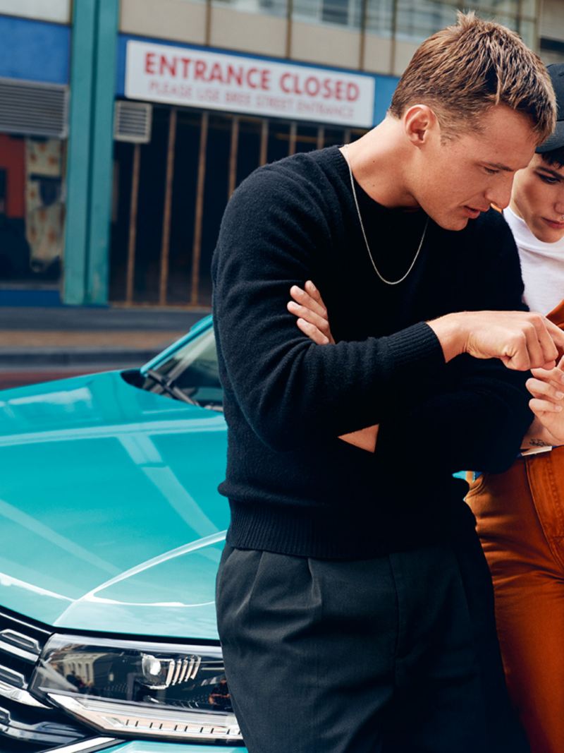 Mies ja nainen seisovat Volkswagen T-Crossin edessä ja selaavat matkapuhelinta
