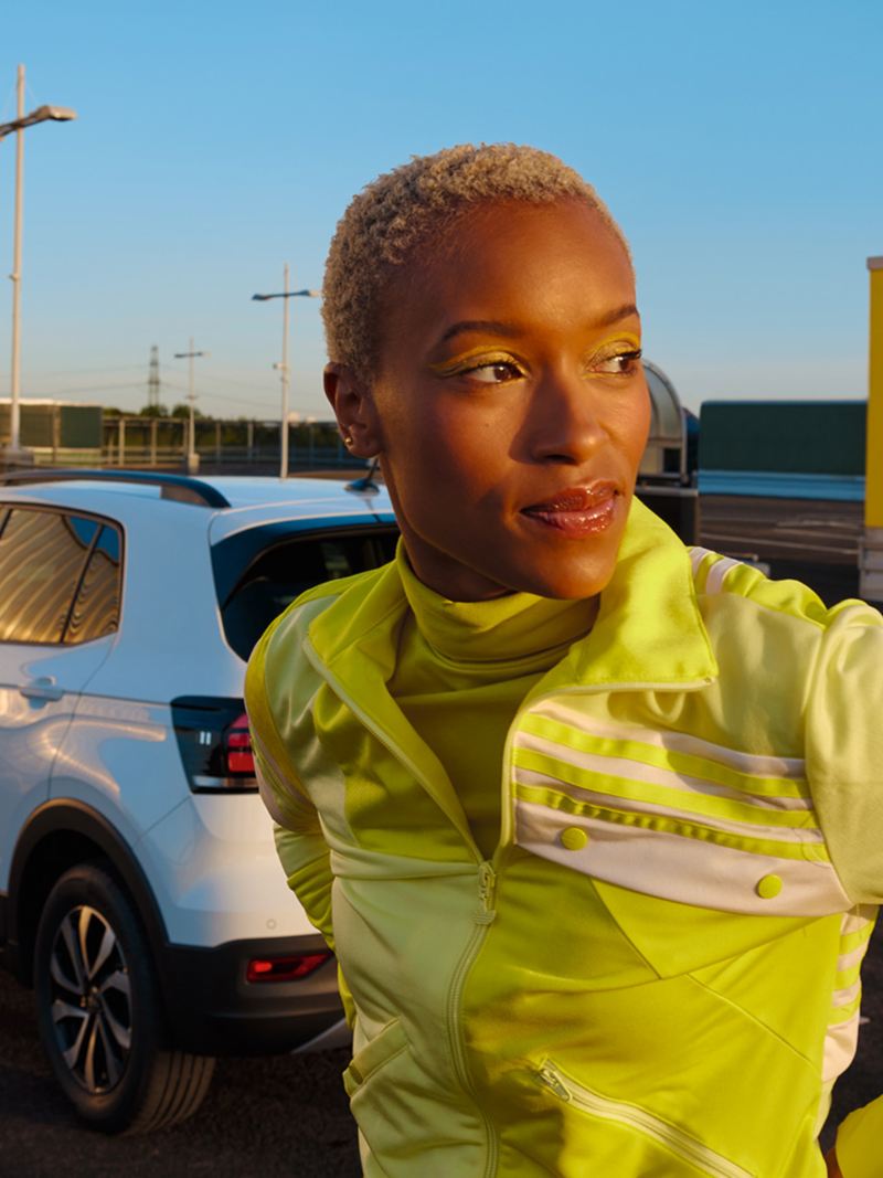 VW T-Cross ACTIVE blanc dans un parking urbain. Une femme en chemise jaune se tient devant celui-ci.