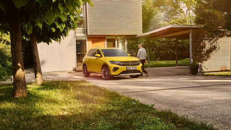 Le VW T-Cross jaune de profil devant un paysage méditerranéen.