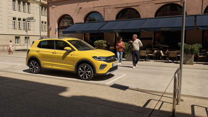 Un VW T-Cross jaune garé sur le côté un face d'un café, un couple descend de la voiture.