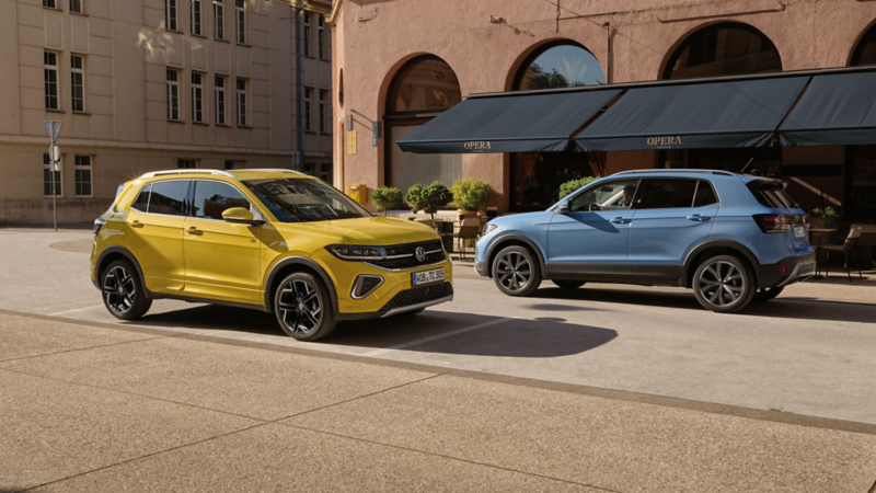 Un VW T-Cross jaune et un bleu se croisent sur une route en ville.