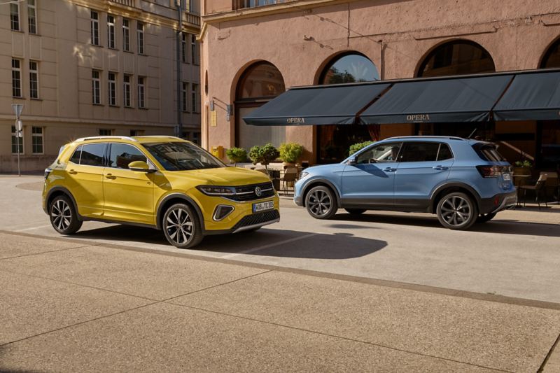 A yellow and a blue VW T-Cross drive past each other on a road in the city.