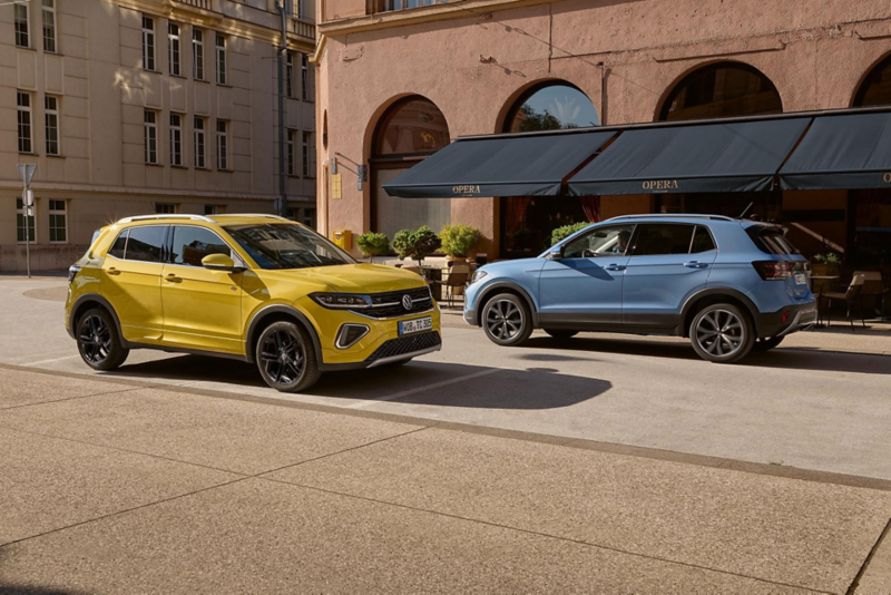 Un VW T-Cross jaune et un bleu se croisent sur une route en ville.