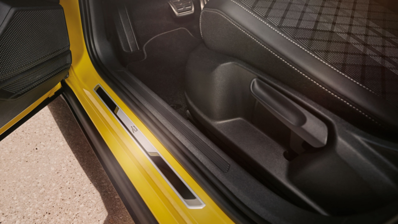 View of the lower part of the driver’s seat of the yellow VW T-Cross with an open front door and a brushed stainless steel door sill.