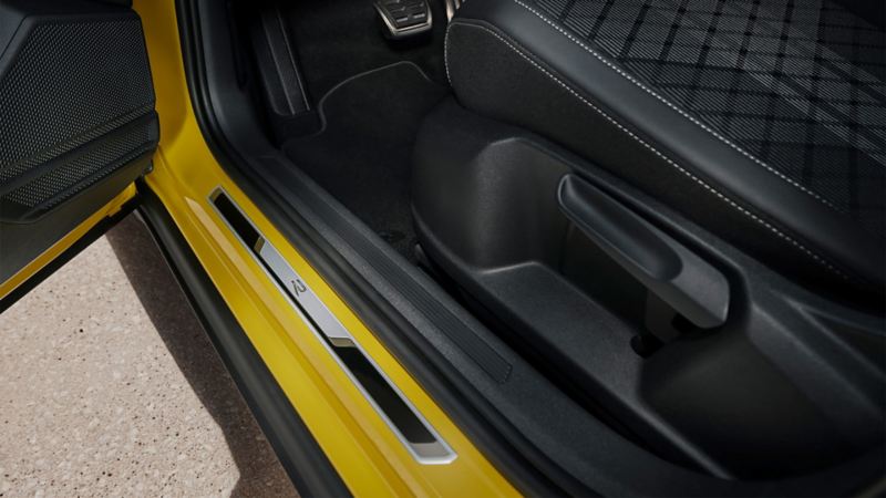 Blik på den nederste del af førersædet i en gul VW T-Cross med åbnet fordør med indstigningsliste i børstet rustfrit stål.