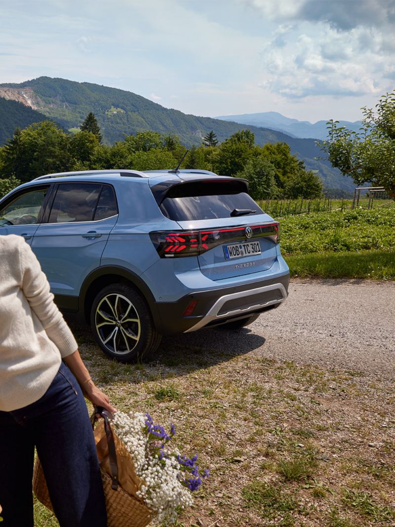 Un uomo e una donna stanno davanti a un chiosco di fiori, dietro di loro una VW T-Cross blu davanti a un paesaggio montuoso.
