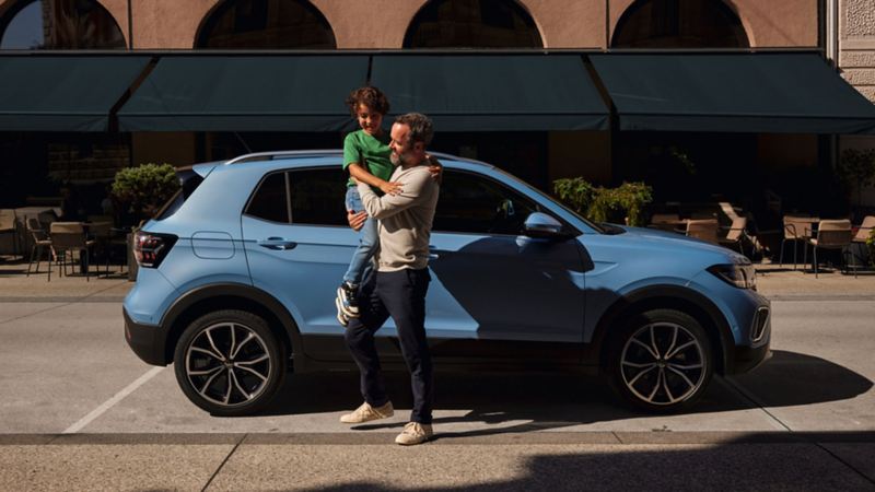 Un uomo tiene un bambino in braccio davanti a una Volkswagen.