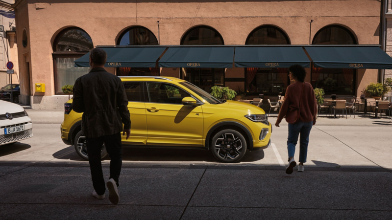 A man and woman approach a yellow VW T-Cross on the side of the road.