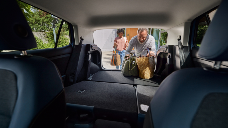 Iemand laadt meerdere tassen in de achterbak van een Volkswagen T-Cross, het shot is vanuit de rijdersstoel