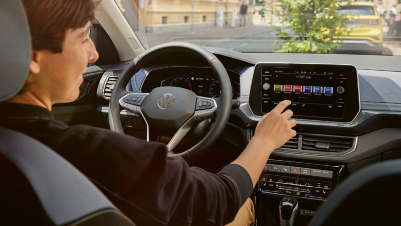 A young woman operates the radio from the driver’s seat via the large display of the infotainment system.