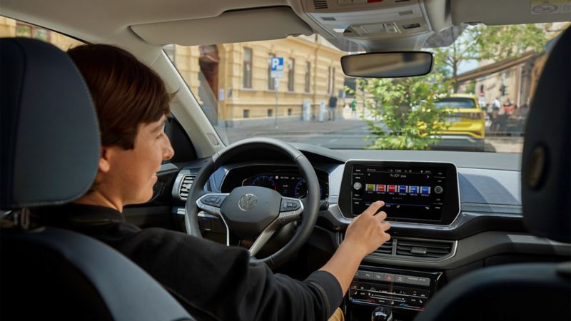 A young woman operates the radio from the driver’s seat via the large display of the infotainment system.