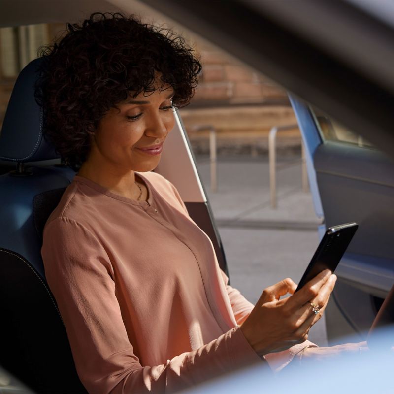 Une femme consulte VW Connect sur son smartphone à l'intérieur d'une Volkswagen.