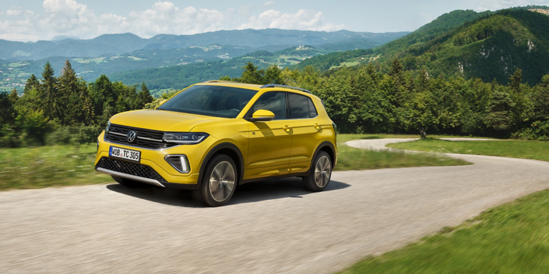 A yellow VW T-Cross on a street in hilly landscape.