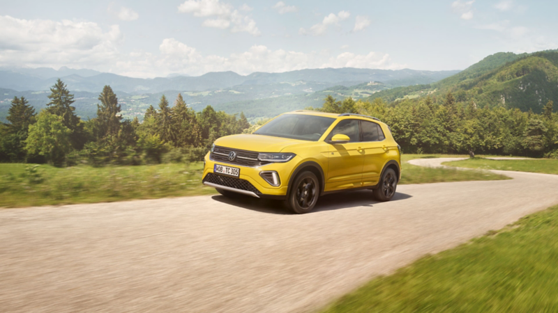 Ein gelber VW T-Cross auf einer Straße in hügeliger Landschaft.