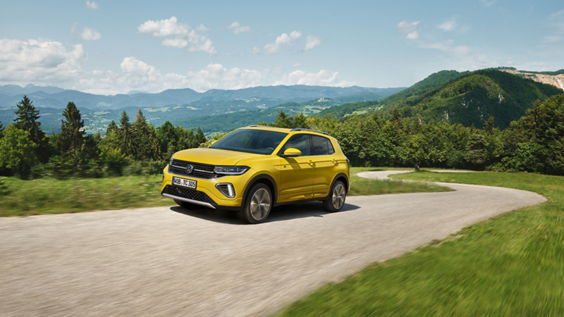 Yellow T-Cross driving up the road, with mountains in the background