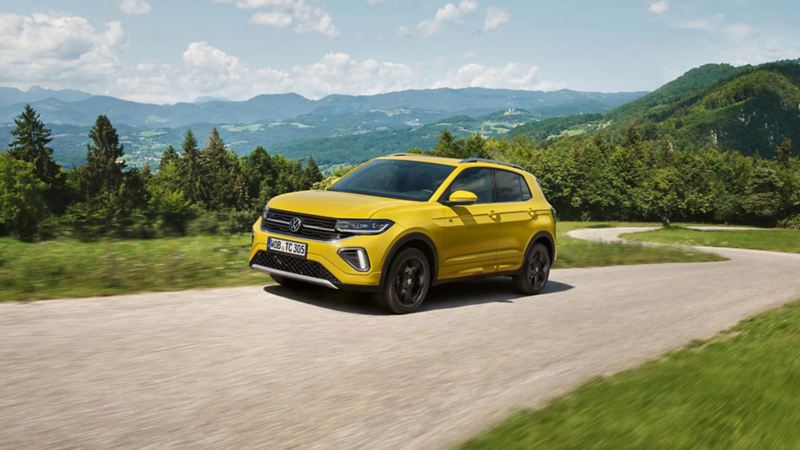 Ein gelber VW T-Cross auf einer Straße in hügeliger Landschaft.