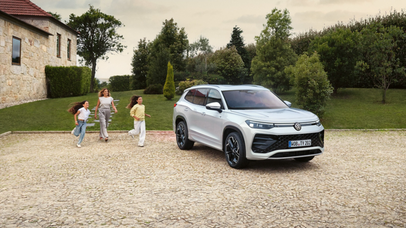 VW Tayron parkt vor einem mediterranen Haus, eine Frau mit zwei Kindern gehen darauf zu.