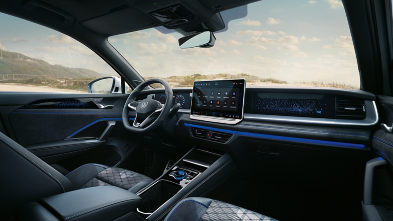 Blick auf das Cockpit mit Lenkrad und Infotainment-System im VW Tayron mit Aussicht auf Dünenlandschaft.