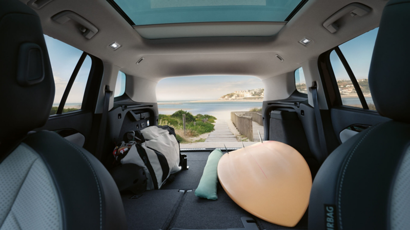 Interior view of the Tayron's boot with rear seats folded down containing a surfboard and a duffle bag