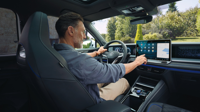 Un homme est assis au volant du VW Tayron et interagit avec le système d'infodivertissement.