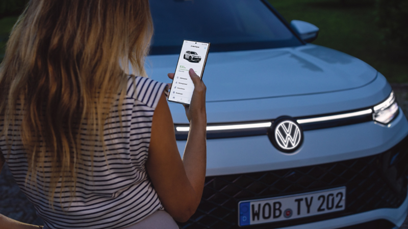 Μία γυναίκα χρησιμοποιεί το VW App στο κινητό της έξω από ένα VW Tayron.