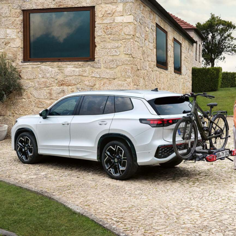 Exterior view of the Tayron parked in the driveway of a home with the towing bracket attached carrying a bike