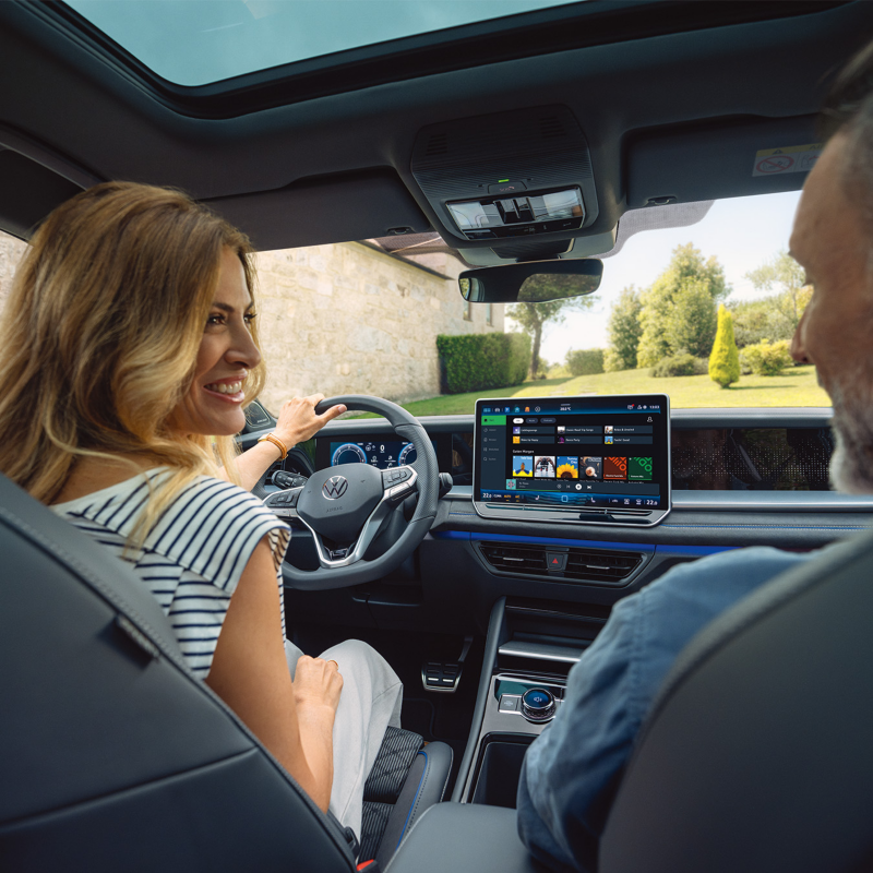 Fahrerin und Beifahrer in einem Volkswagen, Blick auf das digitale Cockpit und das zentrale Infotainment-Display.