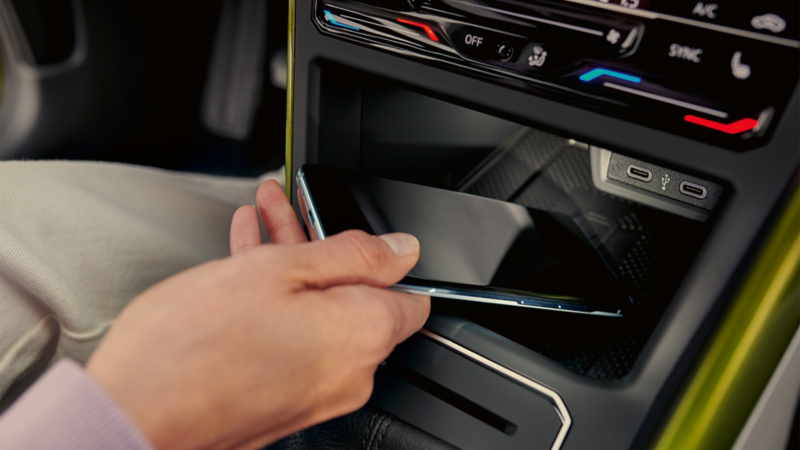Gros plan sur une main qui place un smartphone dans la zone de rangement de la console centrale d'un Volkswagen Taigo, près des ports USB-C.