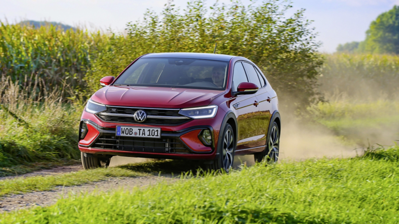 En röd VW Taigo kör längs en grusväg omgiven av grönska