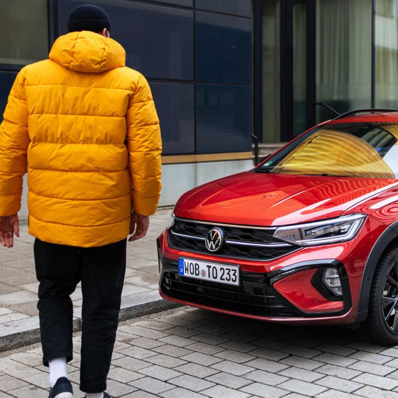 Un homme avec une veste jaune se tient devant une Volkswagen Taigo rouge.