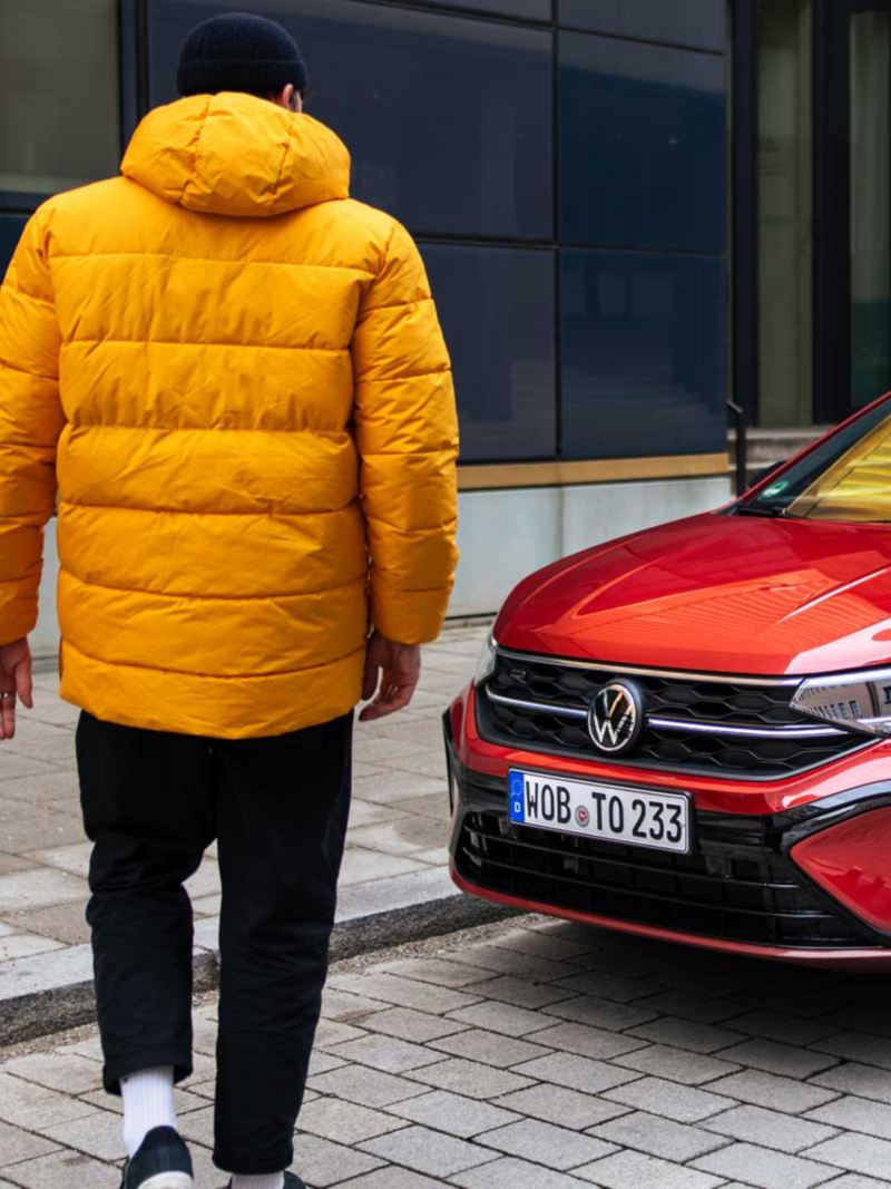 Ein Mann mit gelber Jacke steht vor einem roten Volkswagen Taigo