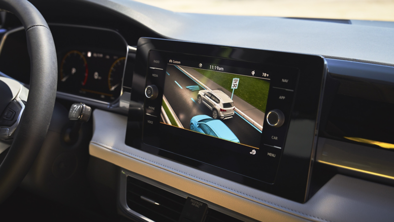 Volkswagen IQ.DRIVE display showing adaptive cruise control, lane assist, and blind spot monitoring on car dashboard..