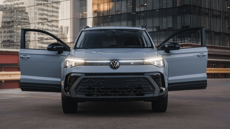 Vue extérieure avant d’un Volkswagen Taos bleu clair stationné dans une rue urbaine moderne, avec les portières avant conducteur et passager ouvertes.