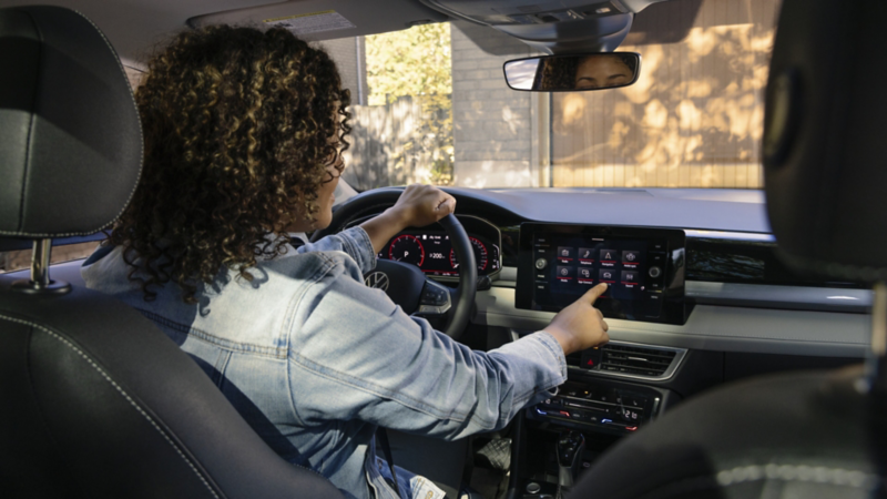 A woman with curly hair sitting in the driver’s seat of a Volkswagen Taos, interacting with the infotainment touchscreen.
