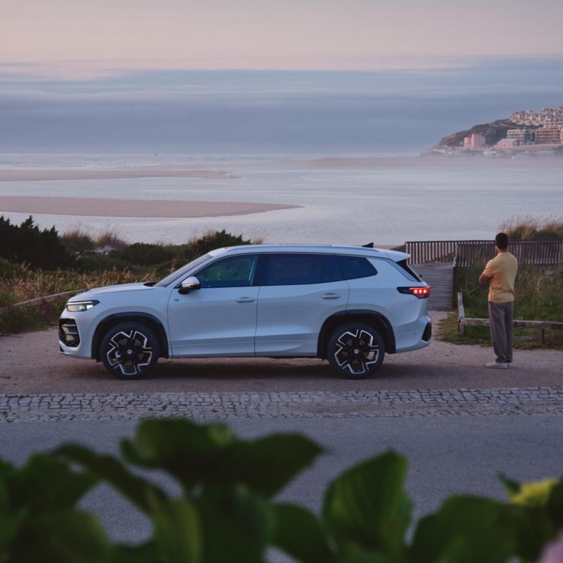 Un Volkswagen Tayron blanco visto de costado aparcado frente al mar