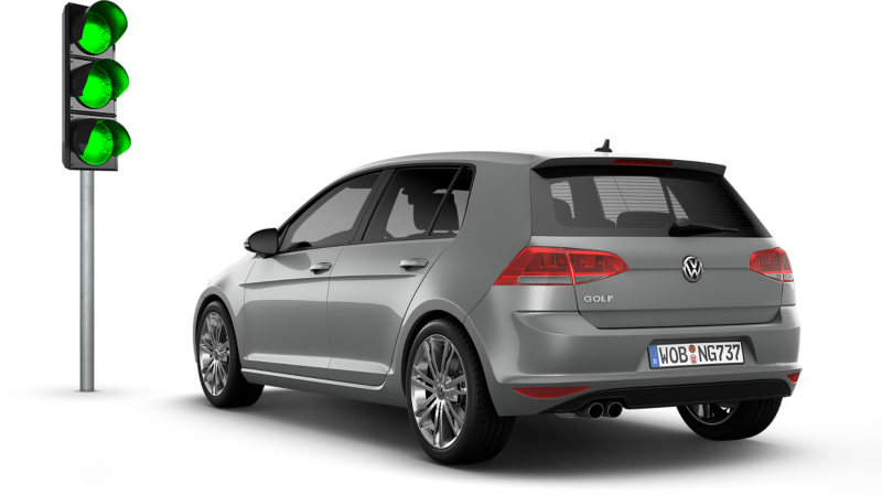 Une Volkswagen Golf gris clair est vue de l'arrière-gauche, garée à côté d'un feu de signalisation vert.