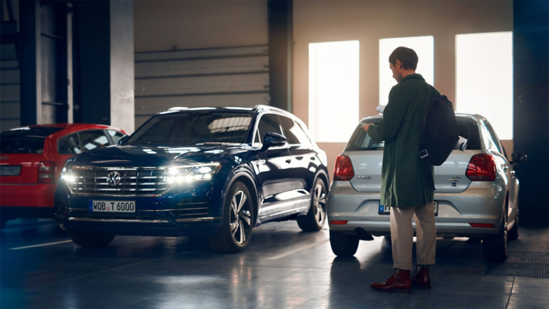 A man stands in a car park in front of three parked Volkswagen
