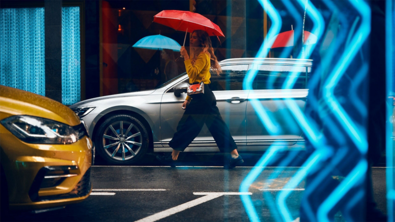 A woman walks by a Volkswagen with an umbrella 