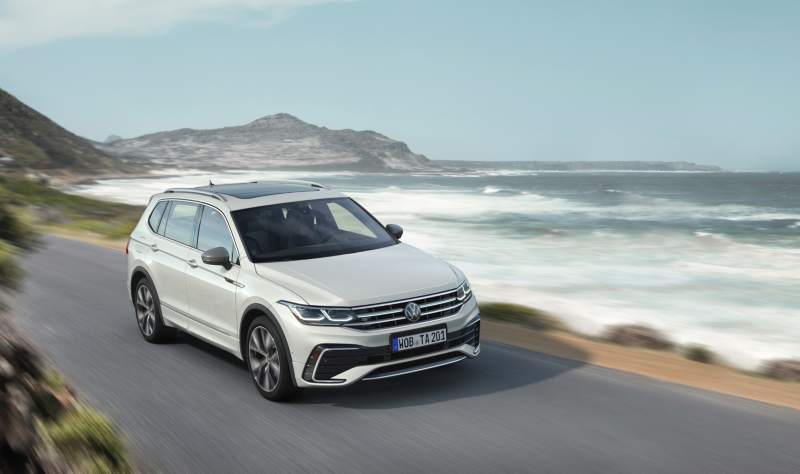 A man leans against the hood of a white Tiguan Allspace R-Line, the LED matrix headlights and light bar on. 