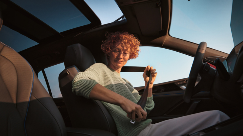 Une femme assise au volant est en train d'attacher sa ceinture.