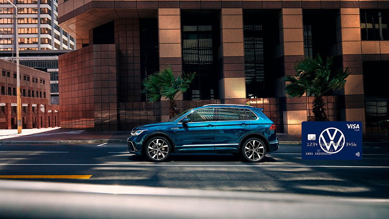 En blå Volkswagen Tiguan parkerad längs en väg utanför ett hus, Volkswagenkortet inklippt i högra hörnet